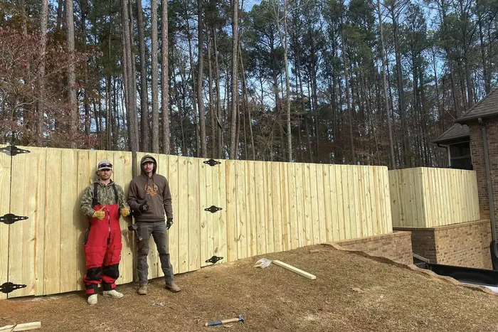Two crew members in front of a finished wood privacy fence in winter