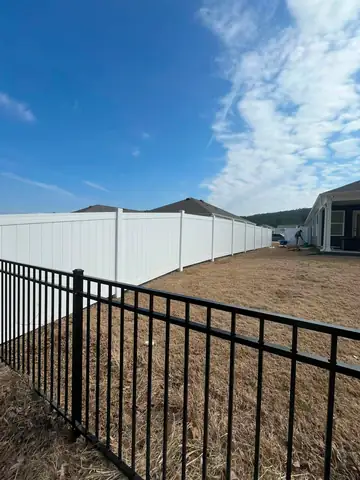White vinyl privacy fence and black aluminum fence at the rear of a house