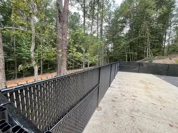 Black chain link fence along a concrete drive in wooded ground