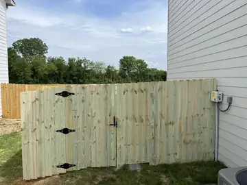 Wood privacy gate with black hardware beside a house