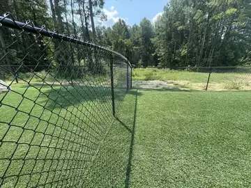 Black chain link fence at the edge of a turf field