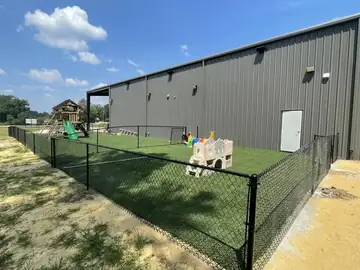 Black chain link fence around a play area beside a metal building