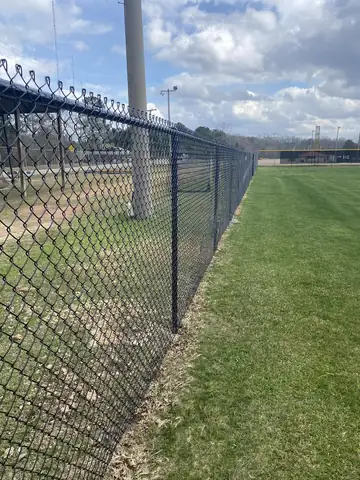 Black chain link fence with barbed top at a sports complex
