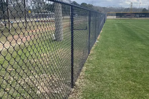 Black chain link fence with barbed top at a sports complex