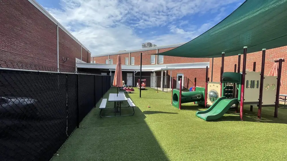 Black chain link fence with privacy screen around a school playground with artificial turf